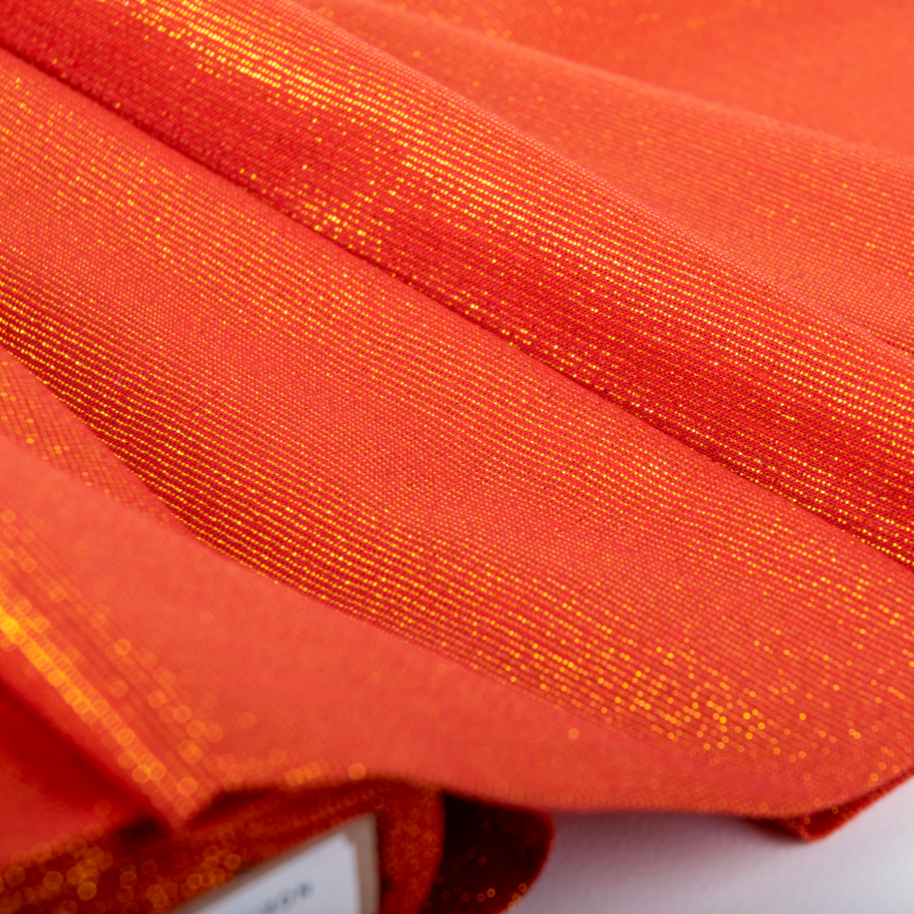 A piece of red gold metallic woven fabric with a close-up texture shot, indicating the fabric's shiny and textured surface.