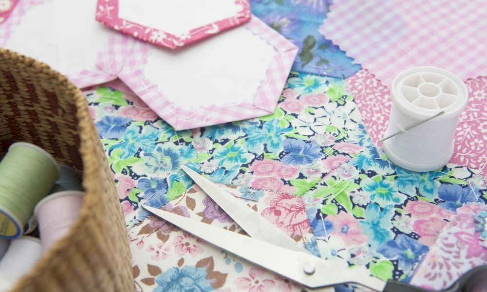 A variety of sewing supplies with quilting tiles in the background.