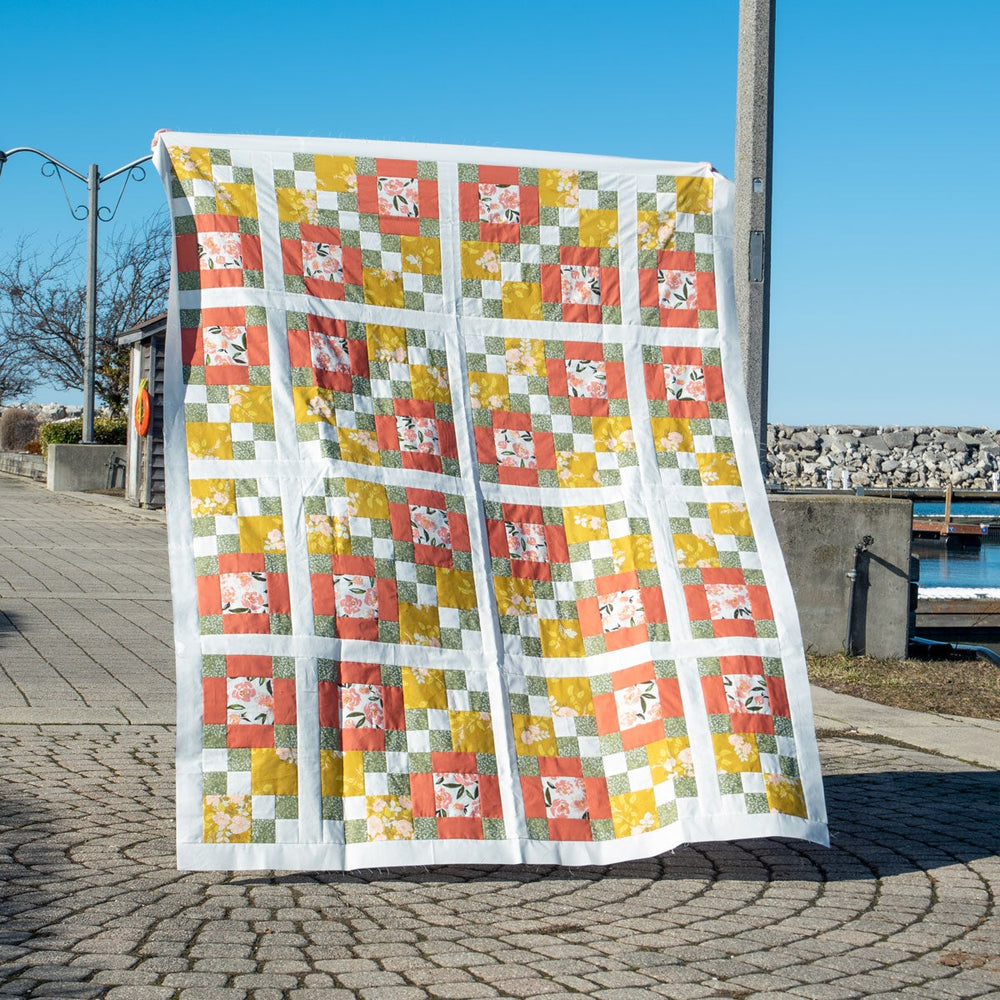 Colourful quilt inspired by traditional 4-patch and 9-patch quilts on a stone pavement near the waterfront