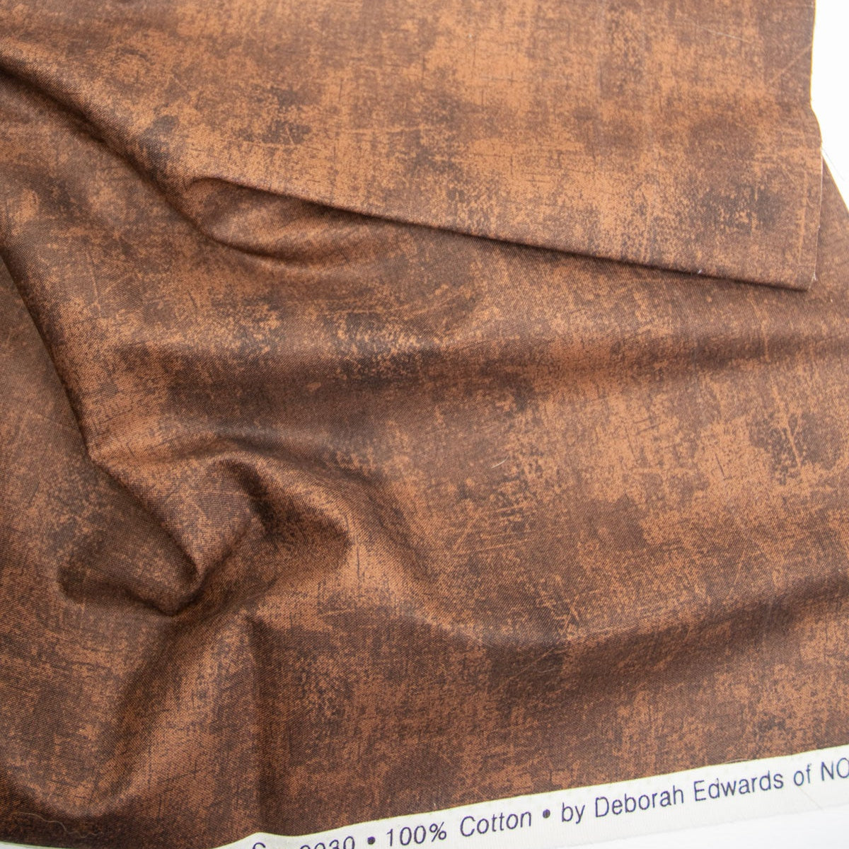 Close-up of brown fabric with visible texture and a label on the selvedge.